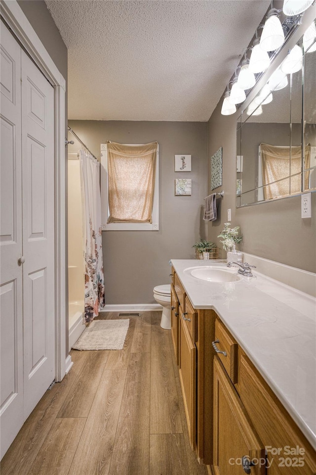 full bathroom featuring toilet, wood finished floors, a textured ceiling, vanity, and a shower stall