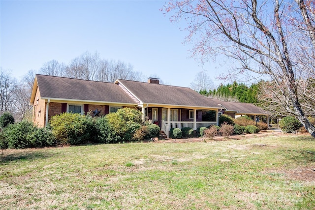 ranch-style house with a porch, roof with shingles, a front yard, brick siding, and a chimney