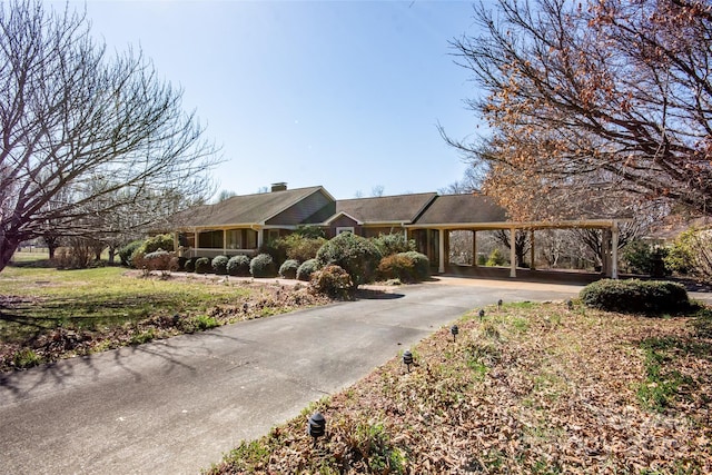 ranch-style house featuring an attached carport, concrete driveway, and a chimney