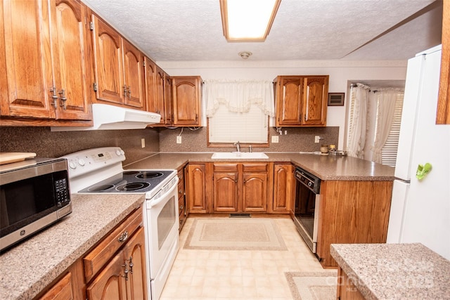 kitchen featuring under cabinet range hood, white appliances, brown cabinets, and a sink