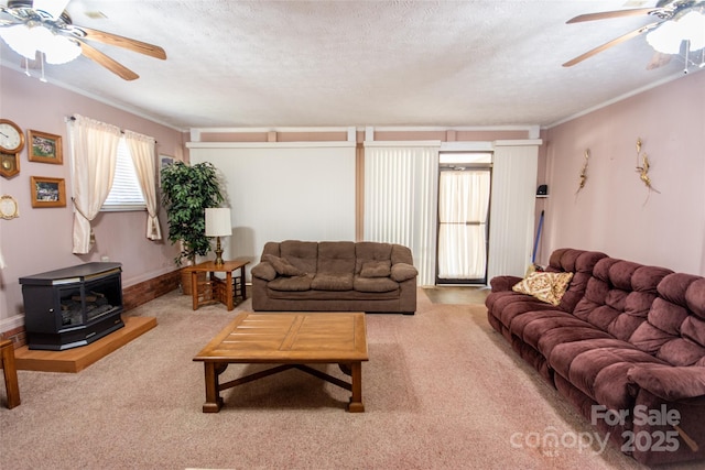 living room featuring crown molding, carpet, a wood stove, a textured ceiling, and a ceiling fan