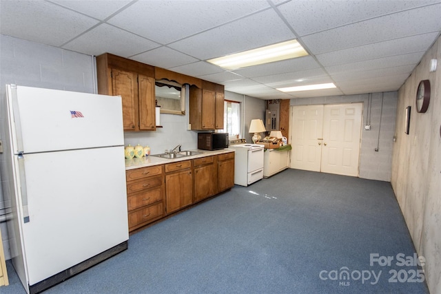 kitchen featuring white appliances, concrete block wall, a sink, light countertops, and brown cabinets