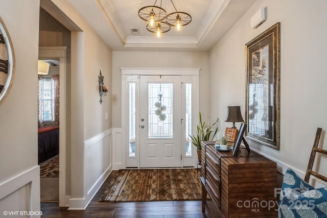 entryway featuring a chandelier, a wainscoted wall, dark wood-type flooring, visible vents, and a tray ceiling