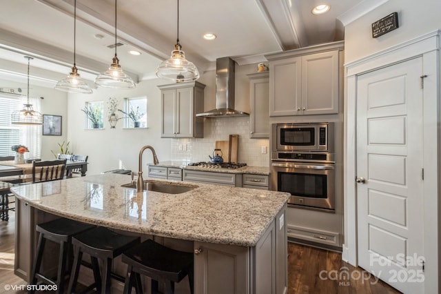 kitchen featuring appliances with stainless steel finishes, a kitchen island with sink, wall chimney range hood, pendant lighting, and a sink