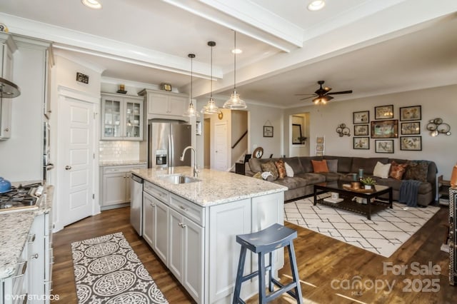 kitchen featuring a sink, open floor plan, appliances with stainless steel finishes, light stone countertops, and an island with sink