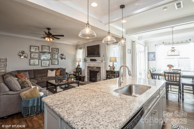 kitchen with a center island with sink, pendant lighting, open floor plan, and light stone counters