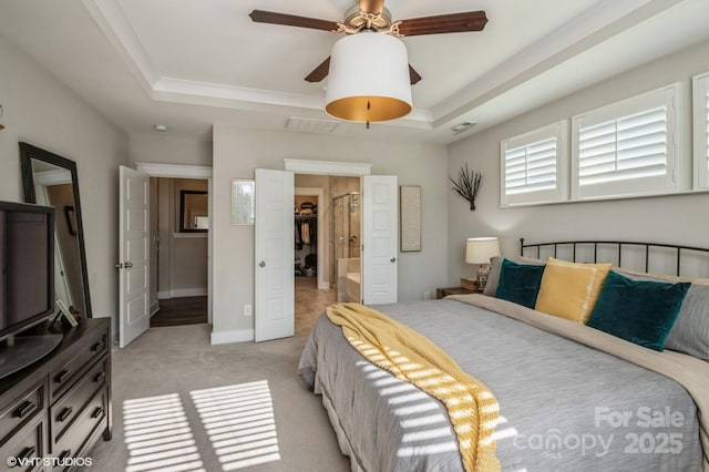 bedroom featuring baseboards, a tray ceiling, ensuite bathroom, and light colored carpet