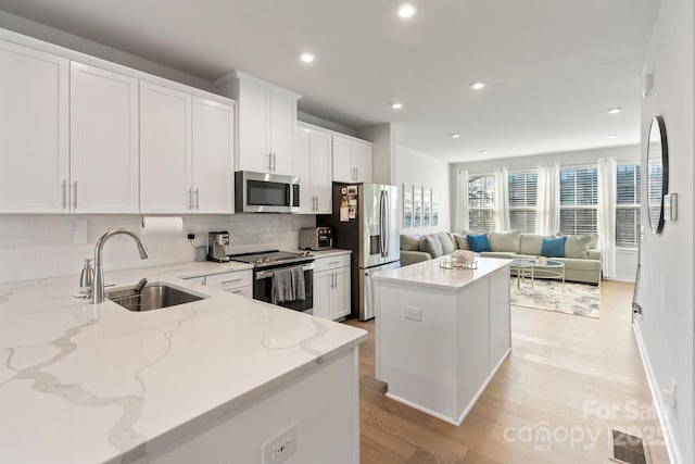 kitchen featuring a sink, appliances with stainless steel finishes, white cabinetry, open floor plan, and a center island