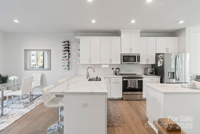 kitchen with light wood finished floors, a kitchen breakfast bar, stainless steel appliances, white cabinetry, and a sink