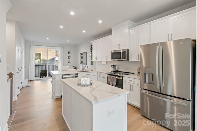 kitchen with tasteful backsplash, a kitchen island, appliances with stainless steel finishes, a peninsula, and a sink