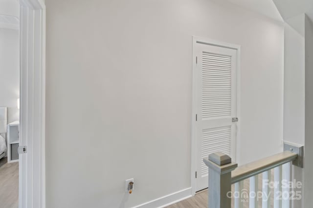 hallway with an upstairs landing, baseboards, and light wood-style floors