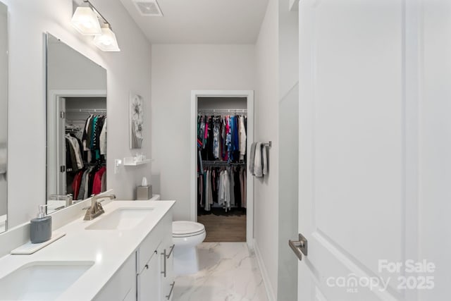 bathroom with visible vents, double vanity, a sink, toilet, and marble finish floor