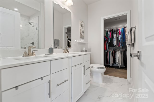 bathroom featuring a sink, a spacious closet, marble finish floor, and a shower stall