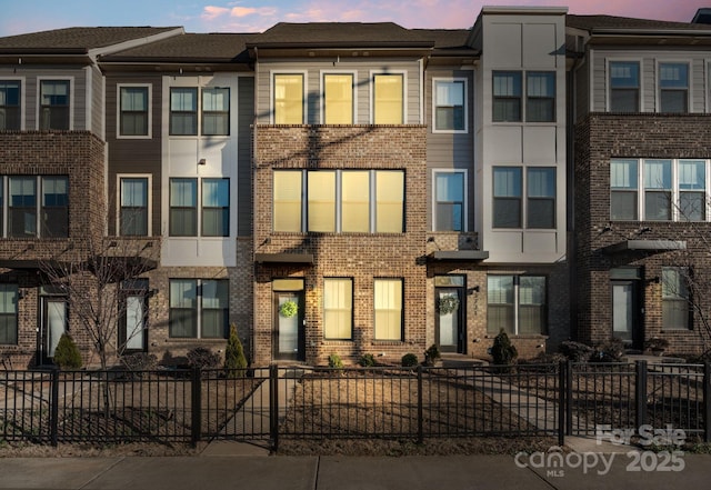 multi unit property with brick siding and a fenced front yard