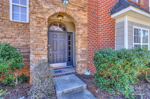 doorway to property featuring brick siding, stone siding, and a shingled roof