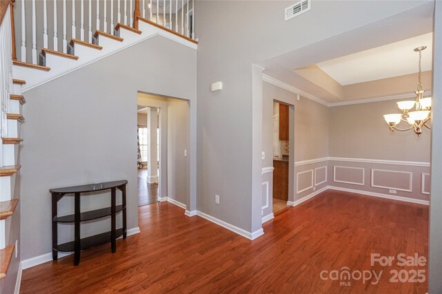 foyer featuring wood finished floors, visible vents, ornamental molding, stairs, and a notable chandelier