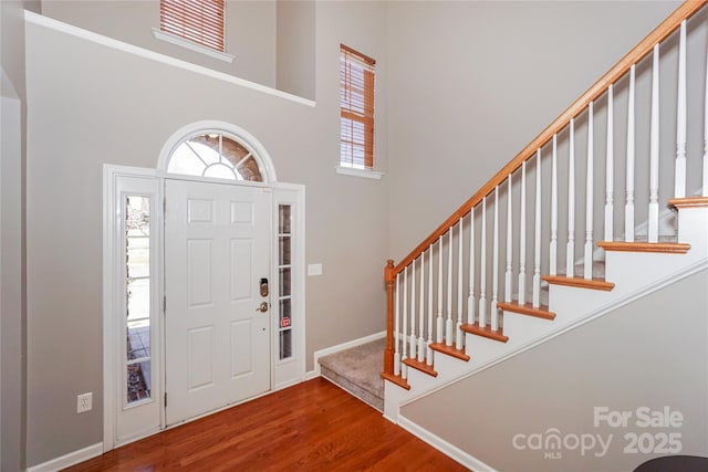 entryway featuring baseboards, stairs, a towering ceiling, and wood finished floors