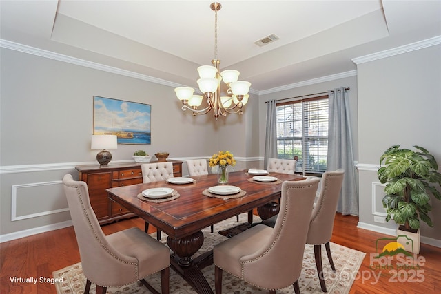 dining space with visible vents, baseboards, an inviting chandelier, wood finished floors, and a raised ceiling