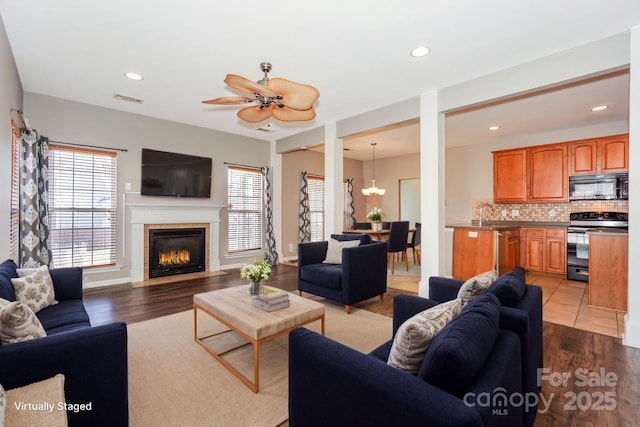 living room featuring visible vents, a tiled fireplace, ceiling fan with notable chandelier, wood finished floors, and recessed lighting