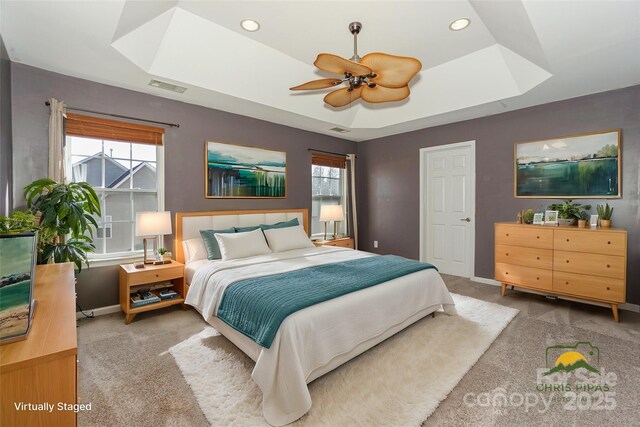 carpeted bedroom featuring a raised ceiling, multiple windows, and baseboards