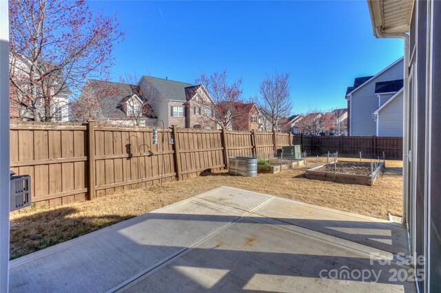 view of yard featuring a residential view, a vegetable garden, a fenced backyard, and a patio