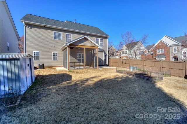 rear view of house with fence, cooling unit, a sunroom, an outbuilding, and a vegetable garden