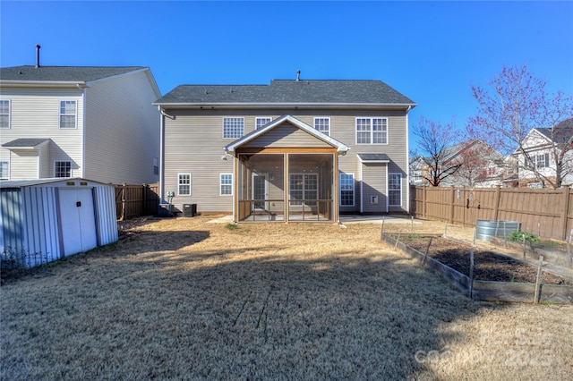 rear view of property with fence, a vegetable garden, a sunroom, an outdoor structure, and a storage unit