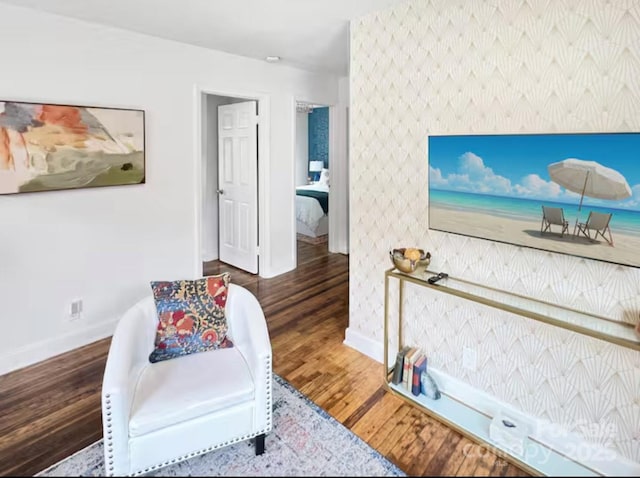 living area with wallpapered walls, wood finished floors, an accent wall, and baseboards