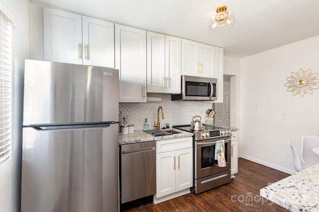 kitchen with a sink, appliances with stainless steel finishes, light stone countertops, tasteful backsplash, and dark wood finished floors