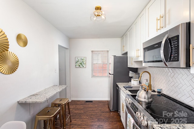 kitchen featuring stainless steel appliances, dark wood-style flooring, white cabinets, light stone countertops, and tasteful backsplash