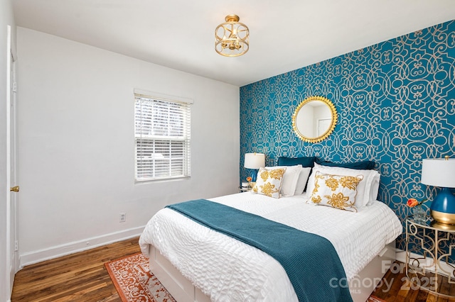 bedroom with baseboards, an accent wall, wood finished floors, and wallpapered walls