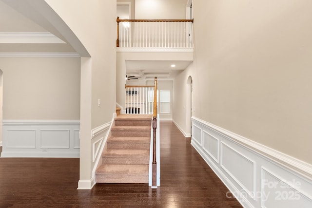 hall with arched walkways, a decorative wall, stairs, dark wood finished floors, and crown molding