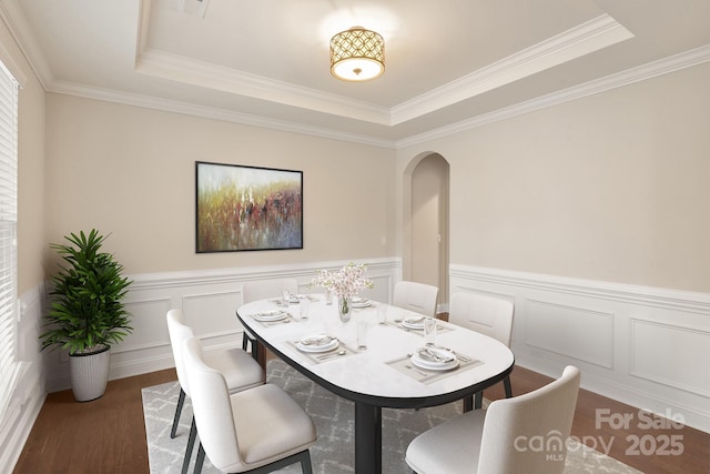 dining area with arched walkways, a decorative wall, dark wood-type flooring, wainscoting, and a tray ceiling