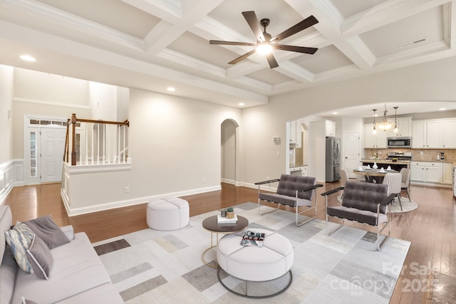 living area with arched walkways, coffered ceiling, visible vents, light wood-style floors, and beamed ceiling