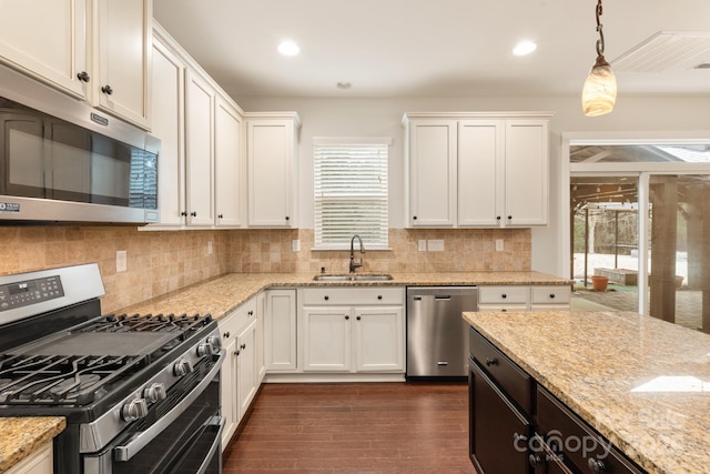 kitchen with hanging light fixtures, appliances with stainless steel finishes, white cabinets, a sink, and light stone countertops