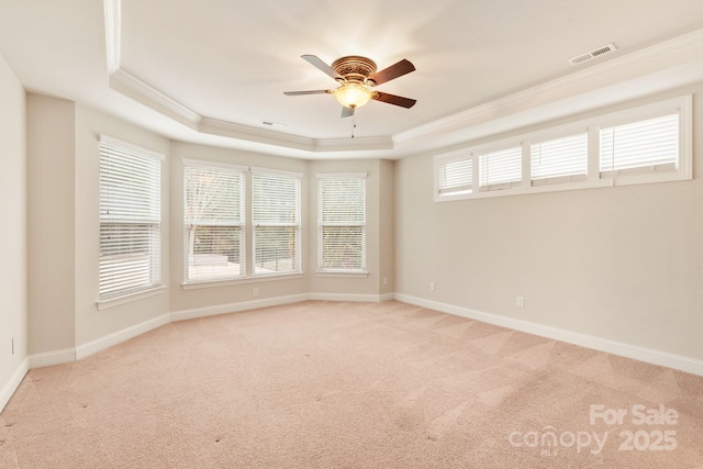 empty room with light carpet, visible vents, a raised ceiling, baseboards, and ornamental molding