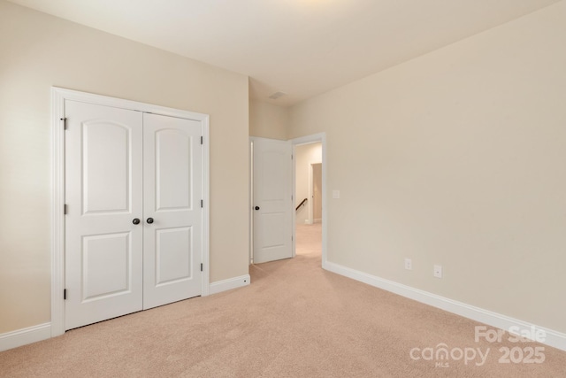 unfurnished bedroom featuring a closet, light colored carpet, and baseboards