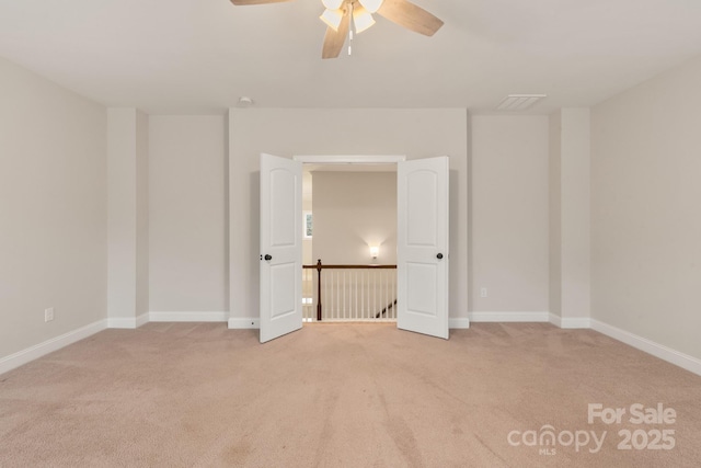 empty room with a ceiling fan, light colored carpet, visible vents, and baseboards