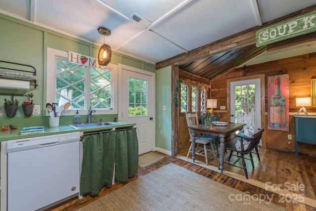 kitchen featuring wooden walls, wood finished floors, white dishwasher, light countertops, and a sink