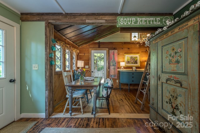 dining room with lofted ceiling, wood walls, wood finished floors, and a notable chandelier