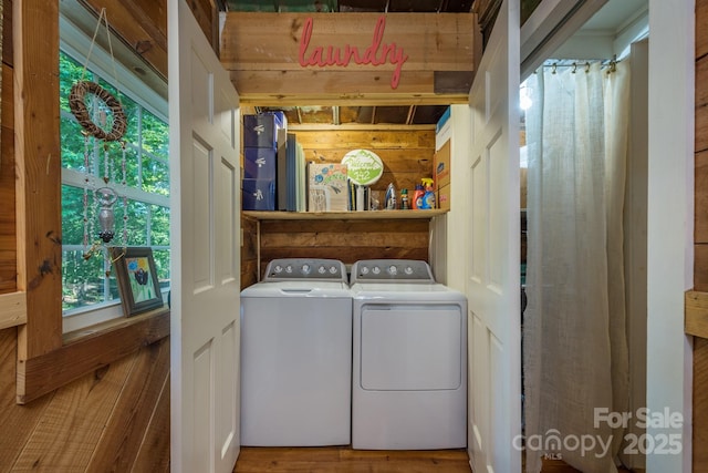 washroom featuring laundry area, washing machine and dryer, wooden walls, and wood finished floors