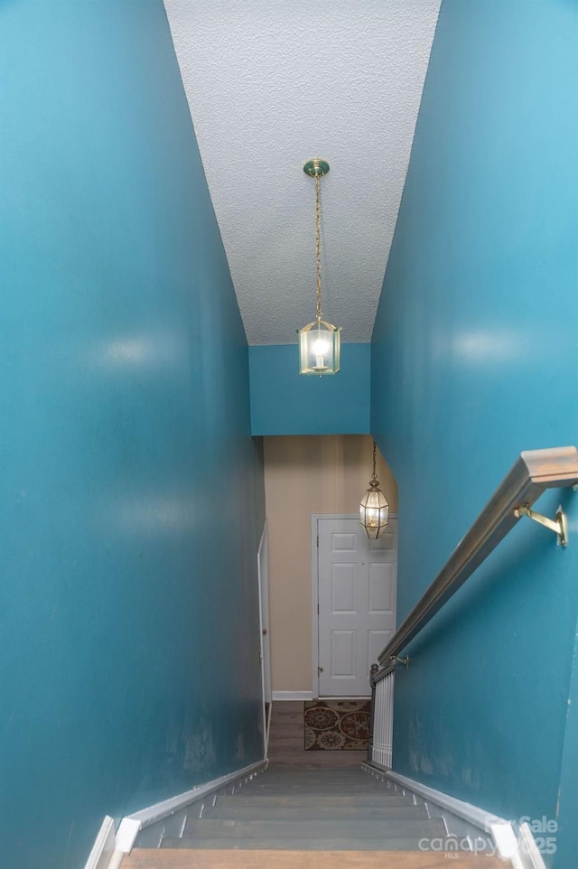 staircase featuring lofted ceiling, a textured ceiling, baseboards, and wood finished floors