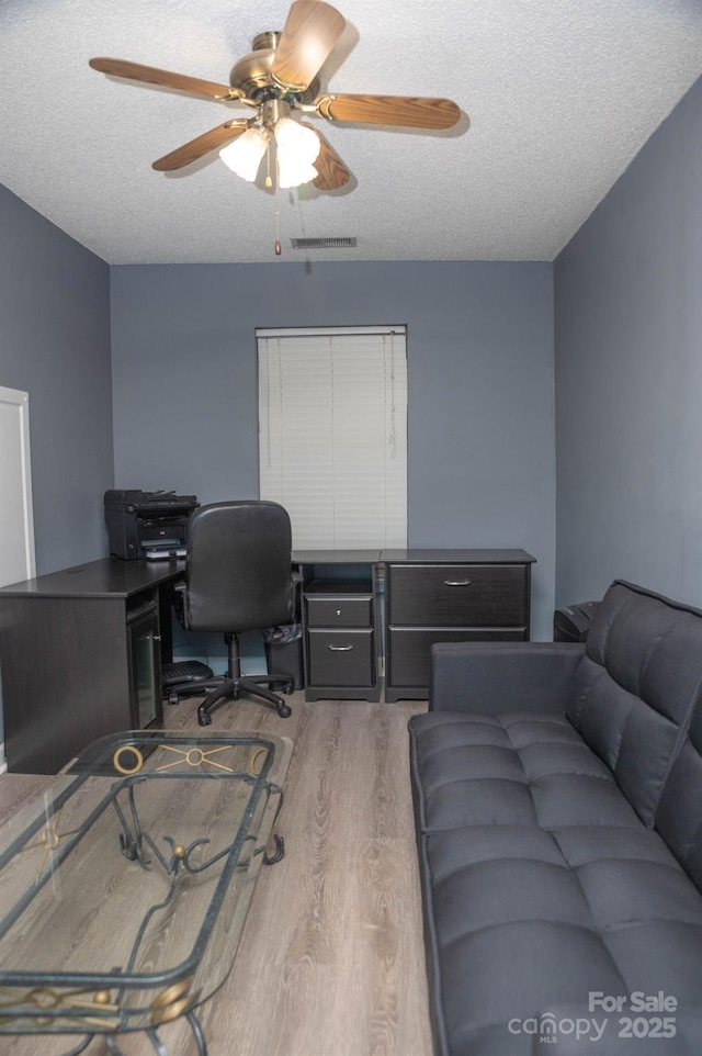 office area with a ceiling fan, a textured ceiling, visible vents, and wood finished floors