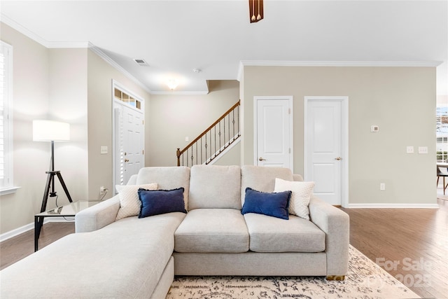 living area featuring baseboards, crown molding, light wood finished floors, and stairs