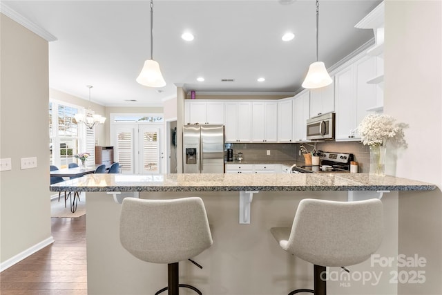 kitchen featuring a peninsula, a breakfast bar, stainless steel appliances, and hanging light fixtures