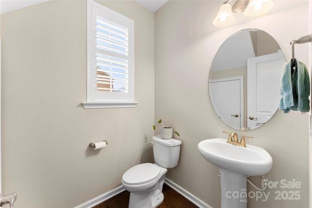 half bath featuring baseboards, a sink, toilet, and wood finished floors