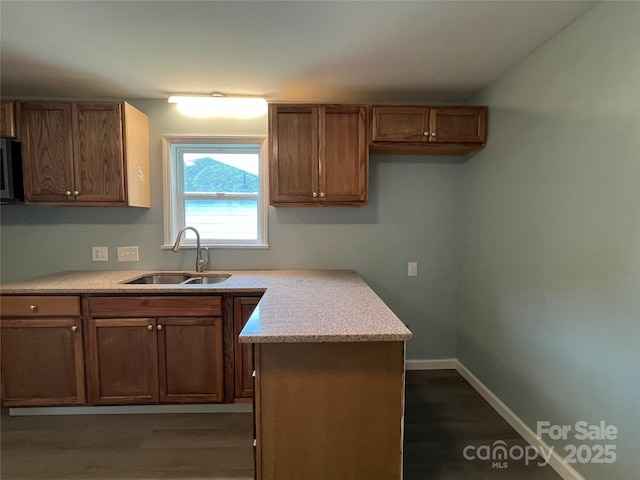 kitchen featuring baseboards, light countertops, a sink, and brown cabinets