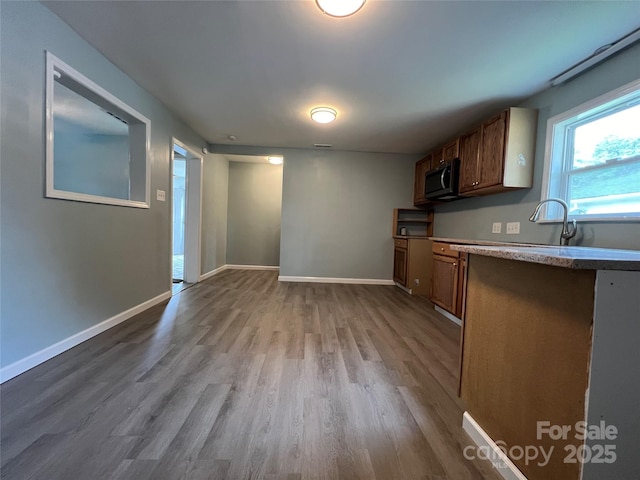 kitchen with light wood finished floors, baseboards, brown cabinets, light countertops, and a sink