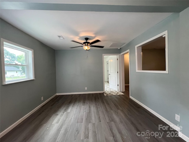 empty room with a ceiling fan, dark wood-style flooring, visible vents, and baseboards