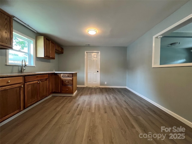 kitchen featuring a sink, baseboards, light countertops, light wood-type flooring, and brown cabinetry